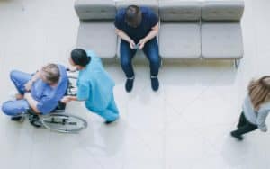man sitting on chair using phone while patients and nurses walking by