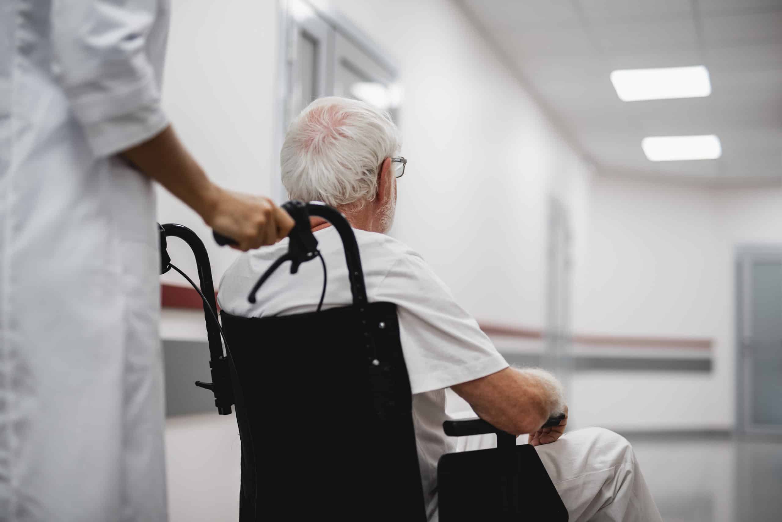 Doctor walking with disabled old man in hospital hallway