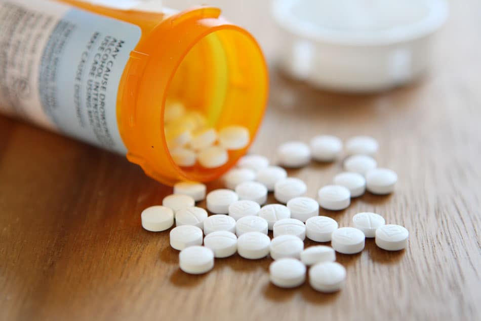 Prescription pill bottle spilling opioids onto table